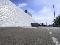 a large white building with a roof of white blocks in the distance is a paved road and trees in front