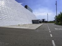 a large white building with a roof of white blocks in the distance is a paved road and trees in front