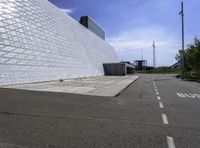 a large white building with a roof of white blocks in the distance is a paved road and trees in front