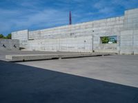 the empty parking lot in front of a wall with apartment buildings on it and a skateboarder on a ramp