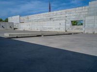 the empty parking lot in front of a wall with apartment buildings on it and a skateboarder on a ramp