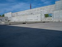 the empty parking lot in front of a wall with apartment buildings on it and a skateboarder on a ramp