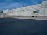 the empty parking lot in front of a wall with apartment buildings on it and a skateboarder on a ramp