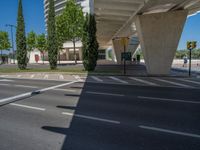 a car sitting at an empty street underneath a overpass overhang that contains a train stop, and cars and a pedestrian