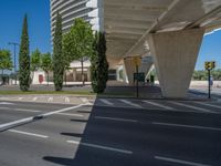 a car sitting at an empty street underneath a overpass overhang that contains a train stop, and cars and a pedestrian