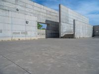 the empty parking lot in front of a wall with apartment buildings on it and a skateboarder on a ramp