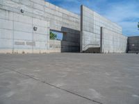 the empty parking lot in front of a wall with apartment buildings on it and a skateboarder on a ramp