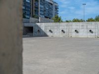 the empty parking lot in front of a wall with apartment buildings on it and a skateboarder on a ramp