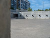 the empty parking lot in front of a wall with apartment buildings on it and a skateboarder on a ramp