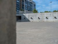 the empty parking lot in front of a wall with apartment buildings on it and a skateboarder on a ramp