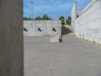 the empty parking lot in front of a wall with apartment buildings on it and a skateboarder on a ramp