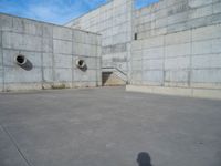 the empty parking lot in front of a wall with apartment buildings on it and a skateboarder on a ramp