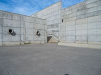 the empty parking lot in front of a wall with apartment buildings on it and a skateboarder on a ramp