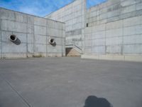 the empty parking lot in front of a wall with apartment buildings on it and a skateboarder on a ramp