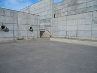 the empty parking lot in front of a wall with apartment buildings on it and a skateboarder on a ramp