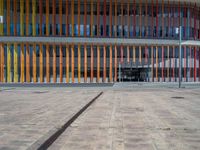 a concrete structure made into rows of orange and yellow poles are on a cement sidewalk