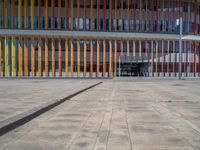 a concrete structure made into rows of orange and yellow poles are on a cement sidewalk