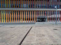 a concrete structure made into rows of orange and yellow poles are on a cement sidewalk