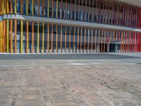 a concrete structure made into rows of orange and yellow poles are on a cement sidewalk