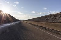 a road running on top of some sand dunes under a blue sky with sun shining