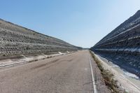 a long empty street leading into an open area next to a water hole on a hill side