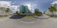 a wide angle fisheye photo shows a blue building in the distance with two bushes and a tree behind