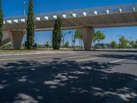 a car sitting at an empty street underneath a overpass overhang that contains a train stop, and cars and a pedestrian