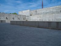 the empty parking lot in front of a wall with apartment buildings on it and a skateboarder on a ramp