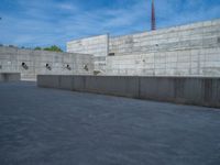 the empty parking lot in front of a wall with apartment buildings on it and a skateboarder on a ramp