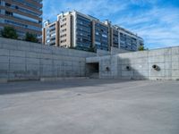 the empty parking lot in front of a wall with apartment buildings on it and a skateboarder on a ramp