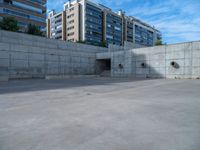 the empty parking lot in front of a wall with apartment buildings on it and a skateboarder on a ramp