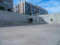 the empty parking lot in front of a wall with apartment buildings on it and a skateboarder on a ramp