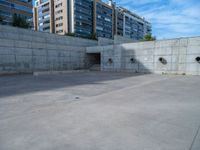 the empty parking lot in front of a wall with apartment buildings on it and a skateboarder on a ramp