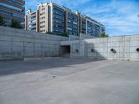 the empty parking lot in front of a wall with apartment buildings on it and a skateboarder on a ramp