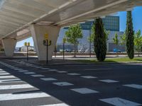 a car sitting at an empty street underneath a overpass overhang that contains a train stop, and cars and a pedestrian