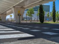 a car sitting at an empty street underneath a overpass overhang that contains a train stop, and cars and a pedestrian