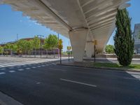 a car sitting at an empty street underneath a overpass overhang that contains a train stop, and cars and a pedestrian