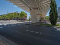 a car sitting at an empty street underneath a overpass overhang that contains a train stop, and cars and a pedestrian