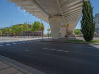 a car sitting at an empty street underneath a overpass overhang that contains a train stop, and cars and a pedestrian