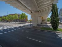 a car sitting at an empty street underneath a overpass overhang that contains a train stop, and cars and a pedestrian