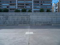 the empty parking lot in front of a wall with apartment buildings on it and a skateboarder on a ramp