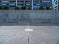 the empty parking lot in front of a wall with apartment buildings on it and a skateboarder on a ramp