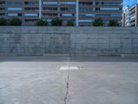 the empty parking lot in front of a wall with apartment buildings on it and a skateboarder on a ramp