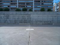 the empty parking lot in front of a wall with apartment buildings on it and a skateboarder on a ramp