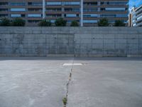 the empty parking lot in front of a wall with apartment buildings on it and a skateboarder on a ramp