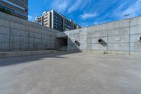 the empty parking lot in front of a wall with apartment buildings on it and a skateboarder on a ramp