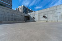 the empty parking lot in front of a wall with apartment buildings on it and a skateboarder on a ramp