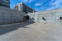 the empty parking lot in front of a wall with apartment buildings on it and a skateboarder on a ramp