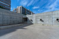 the empty parking lot in front of a wall with apartment buildings on it and a skateboarder on a ramp