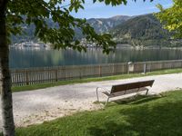 a bench that is sitting on the grass near a river shore and mountains behind it